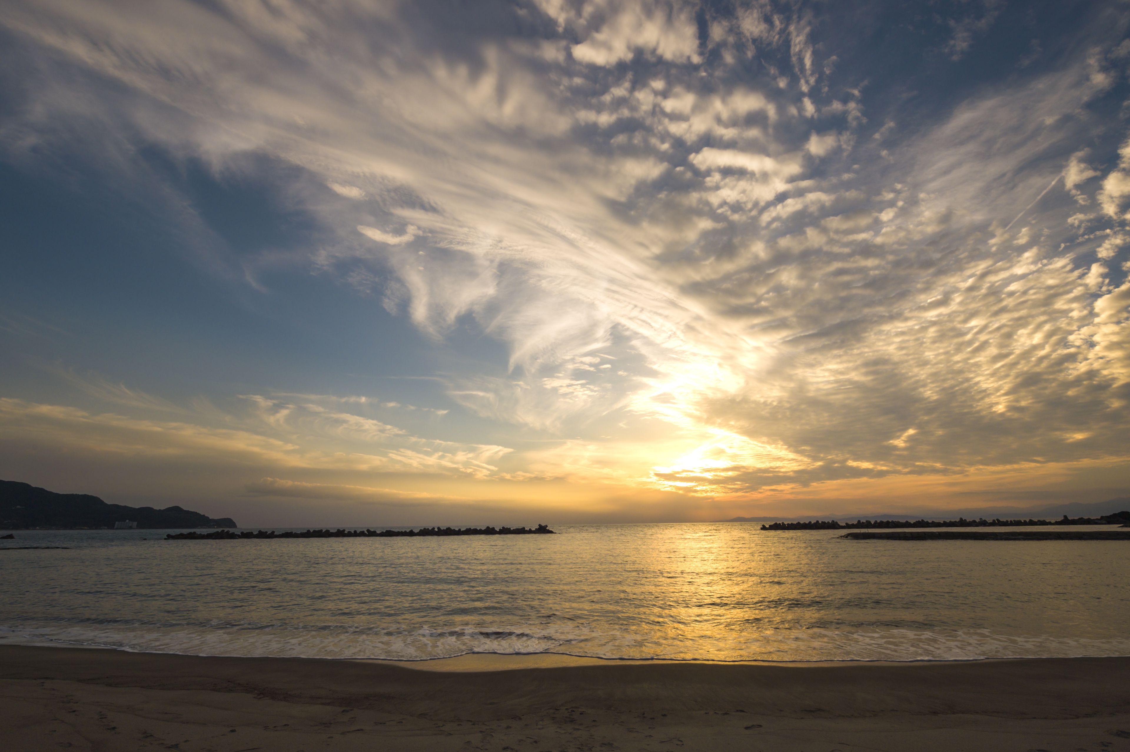 Una playa con atardecer, agua tranquila y montañas al fondo.