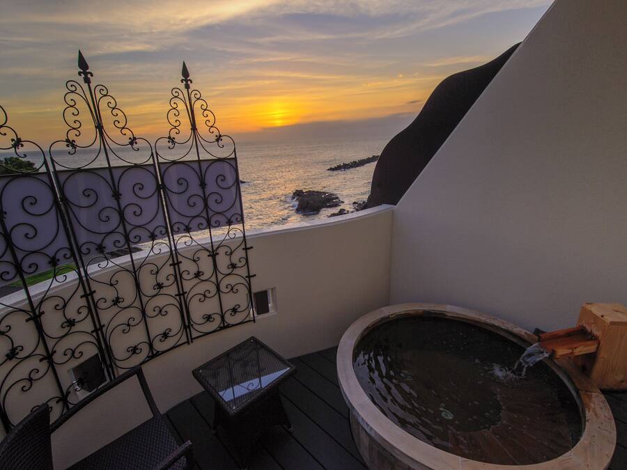 A balcony with a hot tub, a view of the sea, and a decorative metal fence.