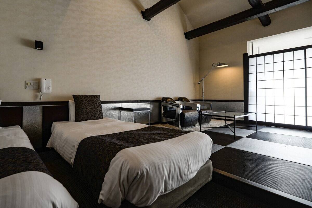 A hotel room with two beds, a desk, a chair, a lamp, and a large window.