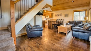 A spacious living area with a wooden staircase, leather sofas, a wooden coffee table, and a kitchen in the background.