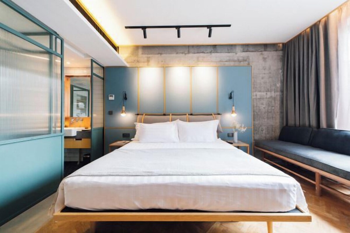 Ett modernt hotellrum med en stor säng, sänglampor, en soffa och utsikt över staden.