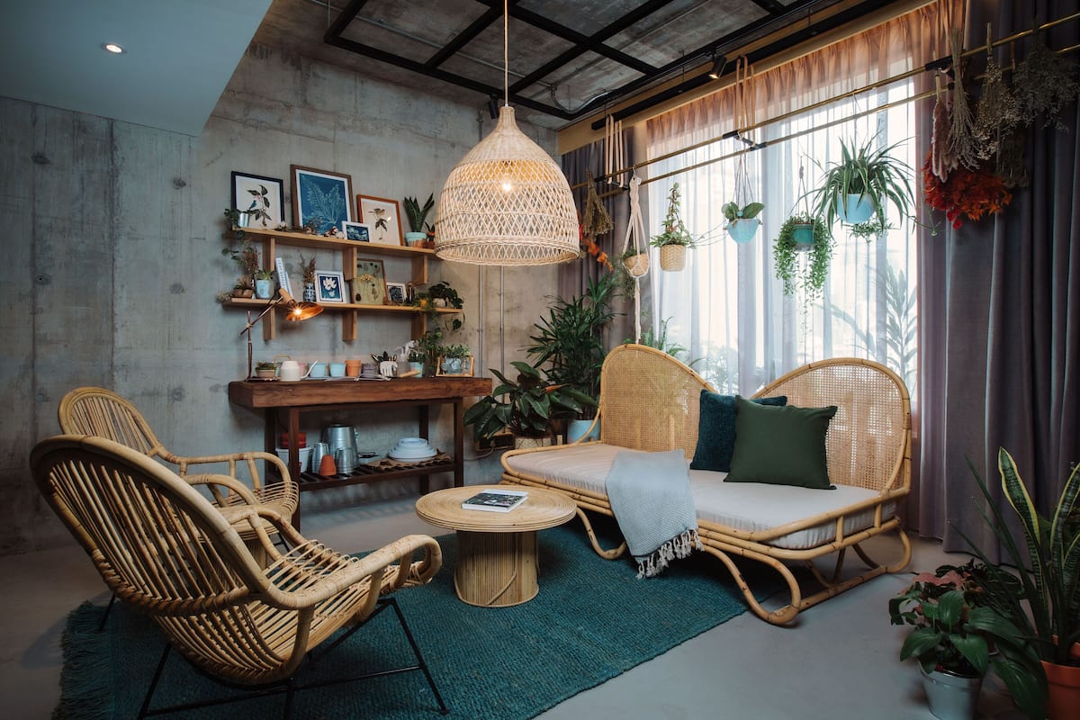 A cozy room with wicker furniture, a hanging light fixture, and various plants.