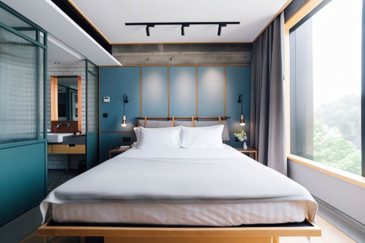 Habitación de hotel moderna con una cama grande, baño con espejo y vistas a zonas verdes.