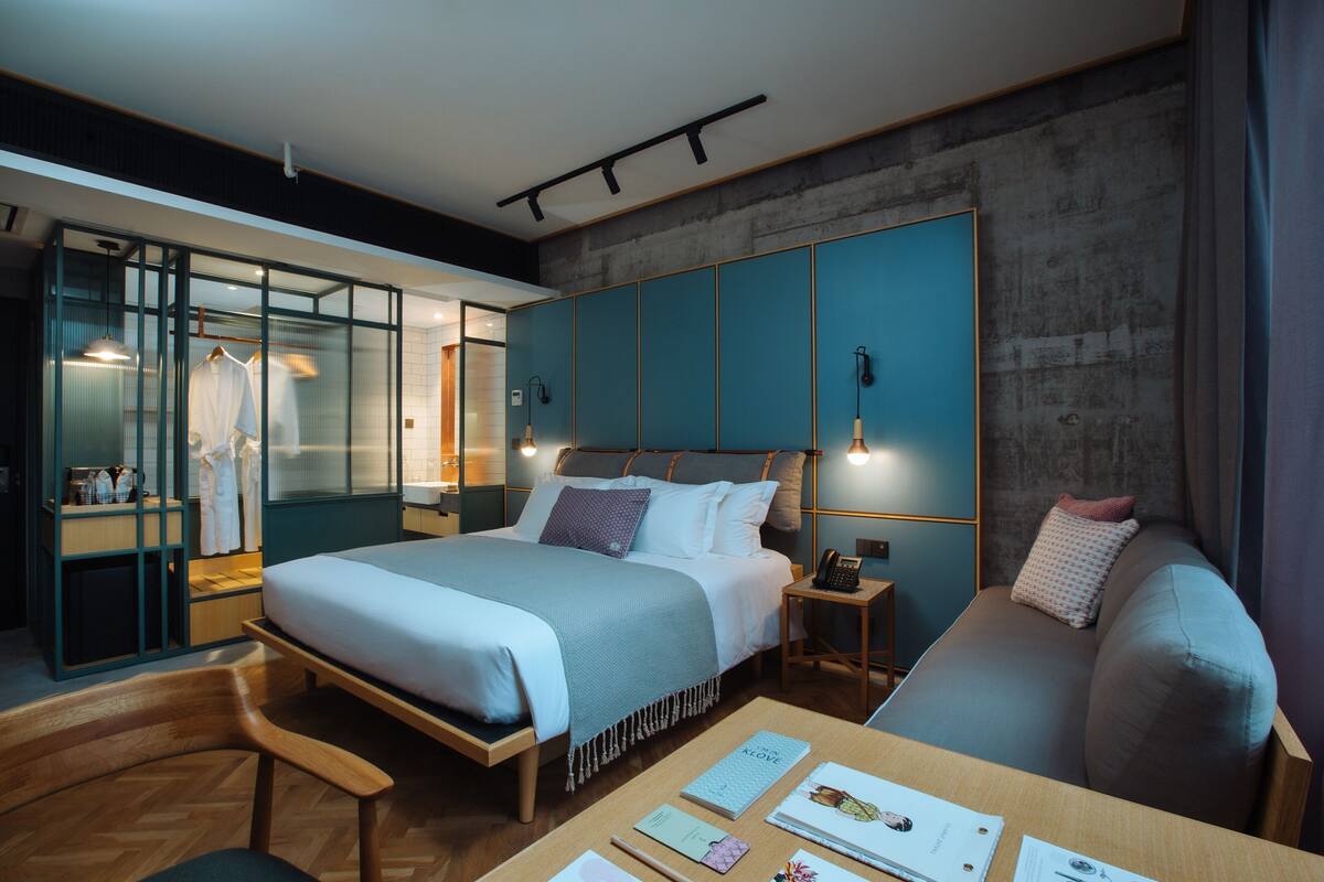 A modern hotel room with a large bed, a seating area, and a desk with a laptop.