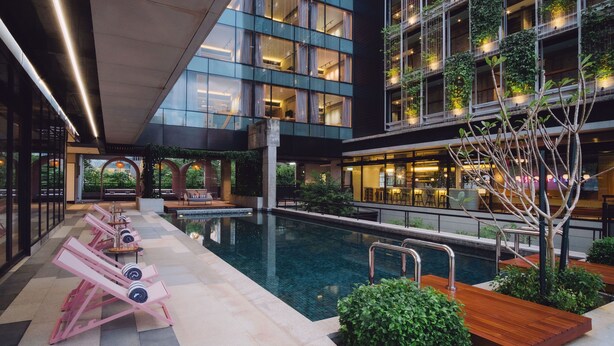 Uma área moderna de piscina interna com espreguiçadeiras, uma piscina pequena e um restaurante com mesas ao ar livre.