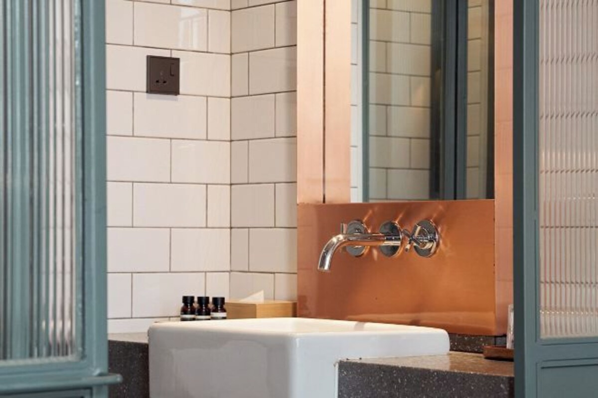 Un baño moderno con azulejos blancos, un lavabo blanco y una cabina de ducha en color cobre.