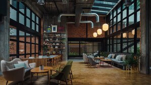 Um interior espaçoso com teto alto, paredes de tijolo aparente, amplas janelas e uma variedade de áreas de estar, incluindo sofás e poltronas.