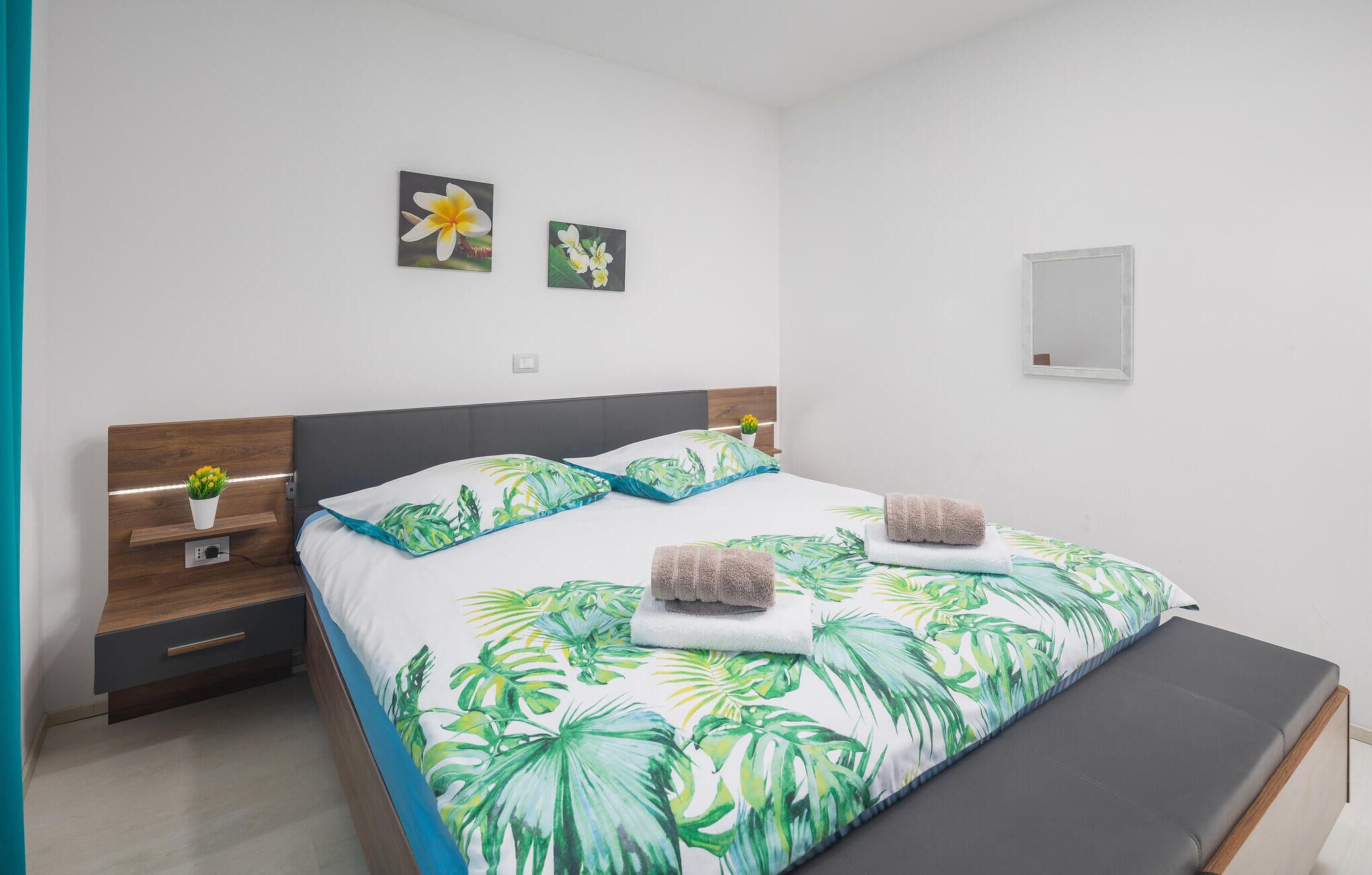 A bedroom with a bed, a bedside table, a bench, and two wall-mounted flower paintings.
