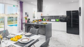 Una cocina moderna con comedor, que presenta suelo de mármol, un refrigerador negro y vistas a una piscina.