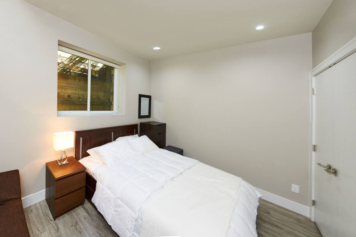 A bedroom with a bed, a nightstand, a bedside table, a window, and a door.
