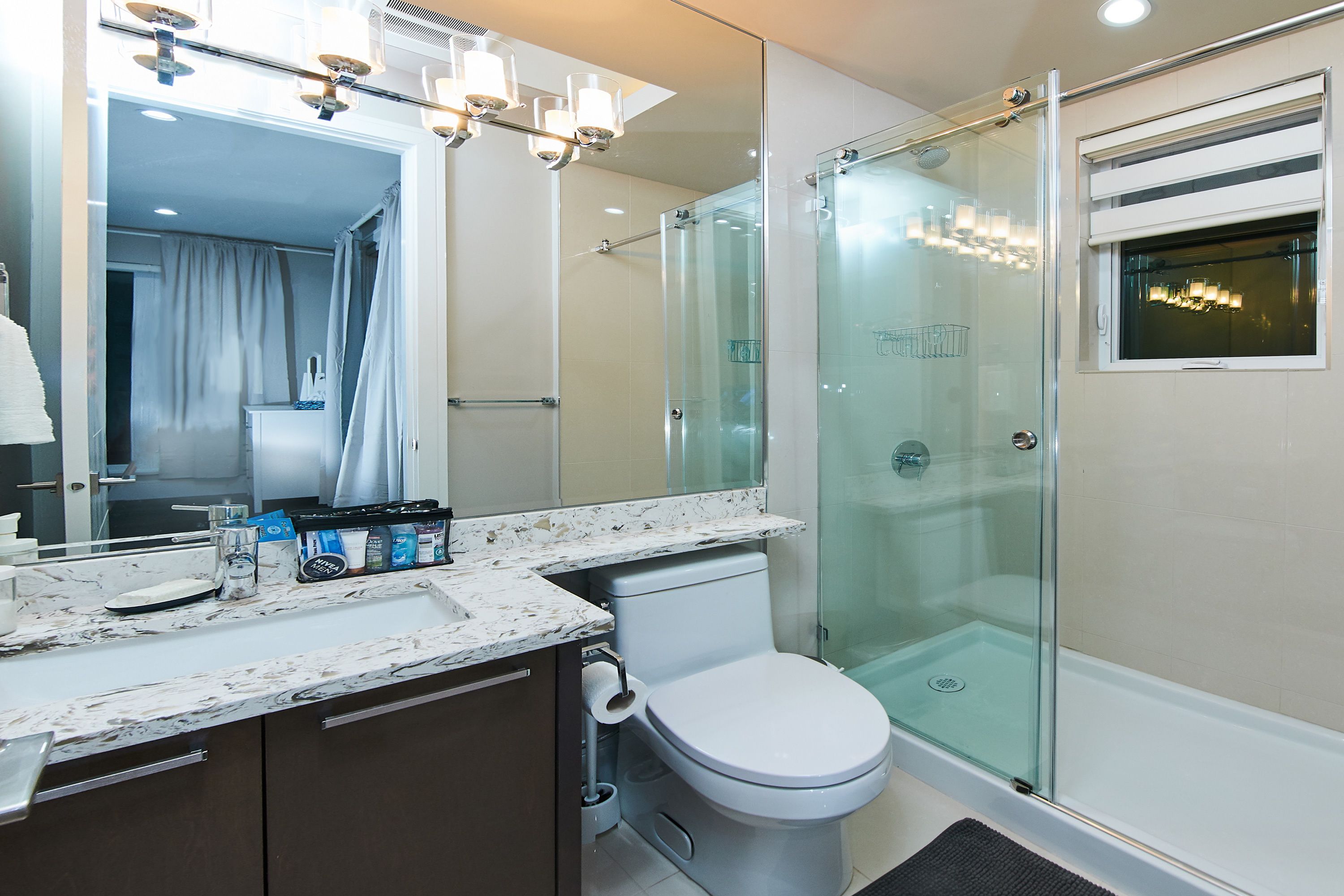 A modern bathroom with a glass-enclosed shower, a white toilet, and a marble countertop.