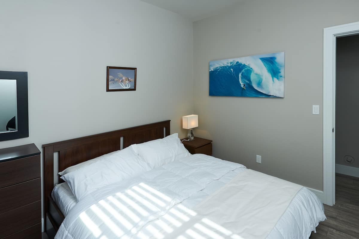 A neatly made bed with white linens, a wooden headboard, a bedside lamp, and a framed picture on the wall.