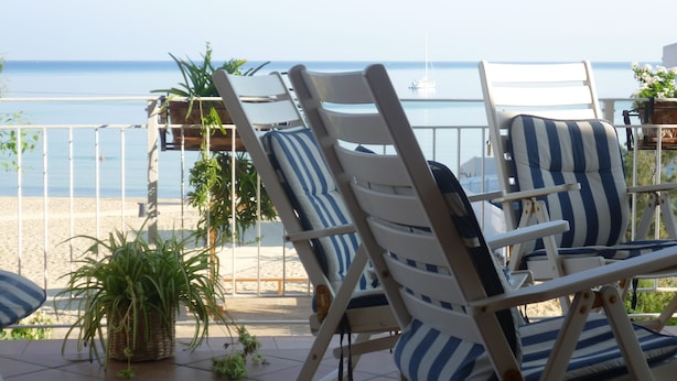En terrasse med liggestole og plantekasser, med udsigt over en strand og havet.