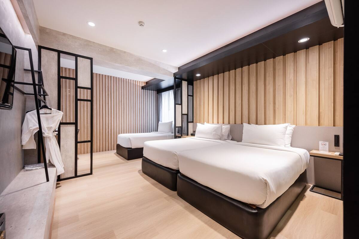 A modern hotel room with a large bed, a separate seating area, and a wooden panel wall.