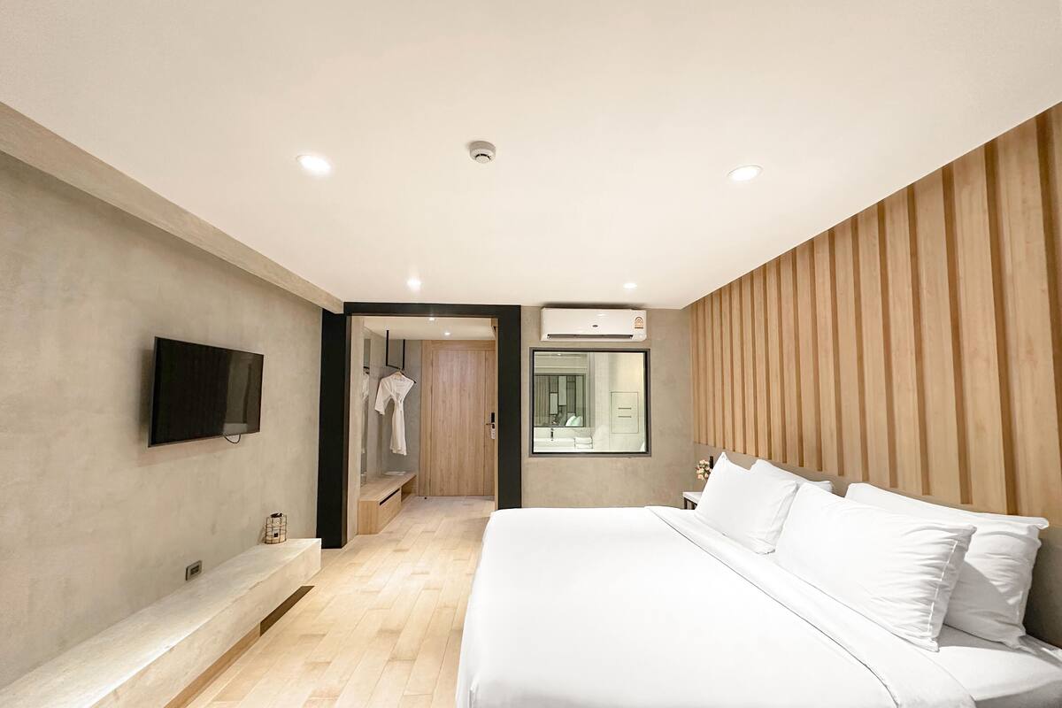A modern bedroom with a large bed, a flat-screen TV mounted on the wall, and a wooden panel wall.