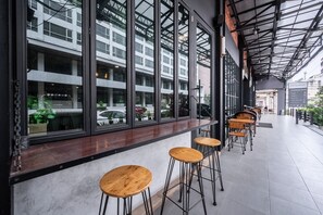 A modern cafe with large windows, wooden stools, and a tiled floor. - Loft Bangkok Hotel (Bangkok)