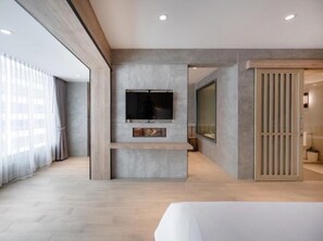 A modern hotel room with a large TV mounted on a grey wall, a wooden floor, and a large window with curtains. - Loft Bangkok Hotel (Bangkok)