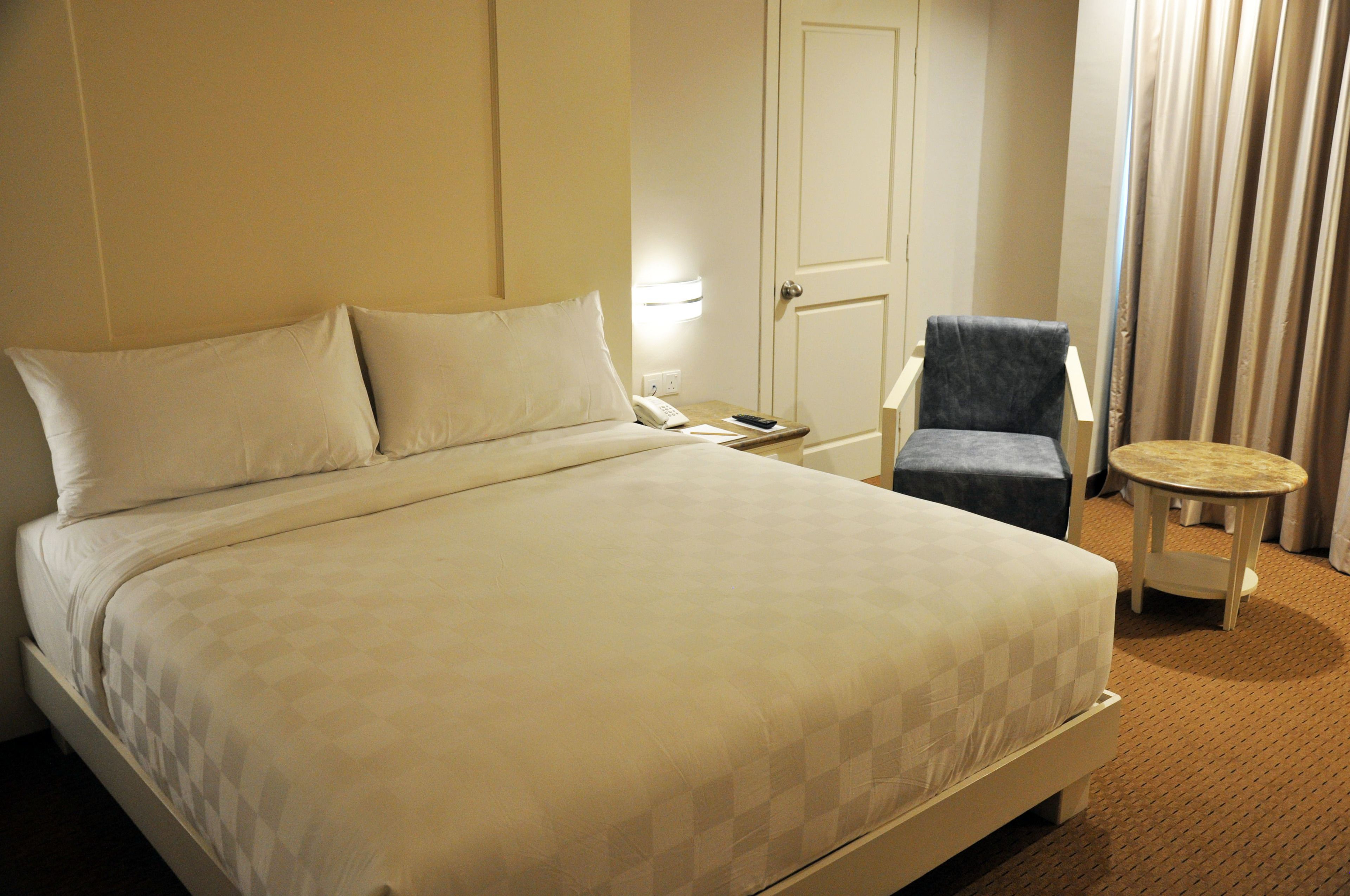 A hotel room with a large bed, a bedside table with a lamp, a chair, and a small round table.