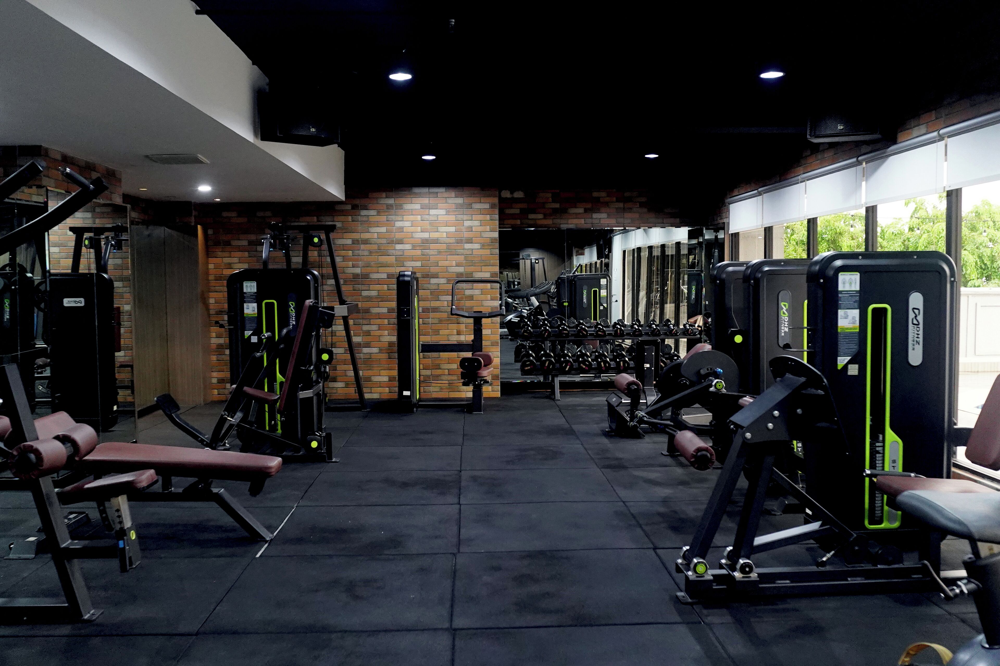 A gym with various exercise machines, a brick wall, and a window providing natural light.