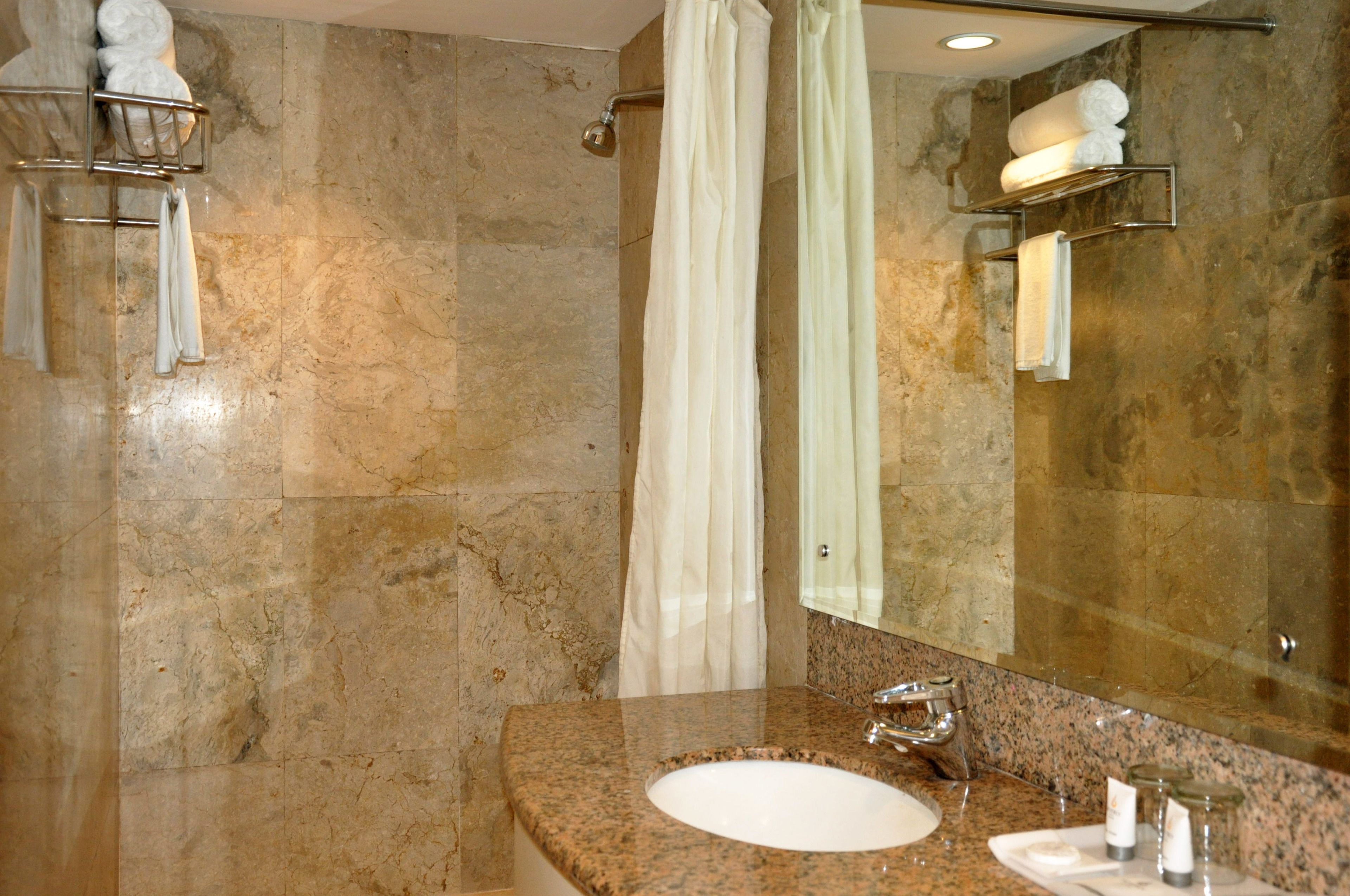 A bathroom with a granite countertop, a sink, a mirror, and a shower with a curtain.