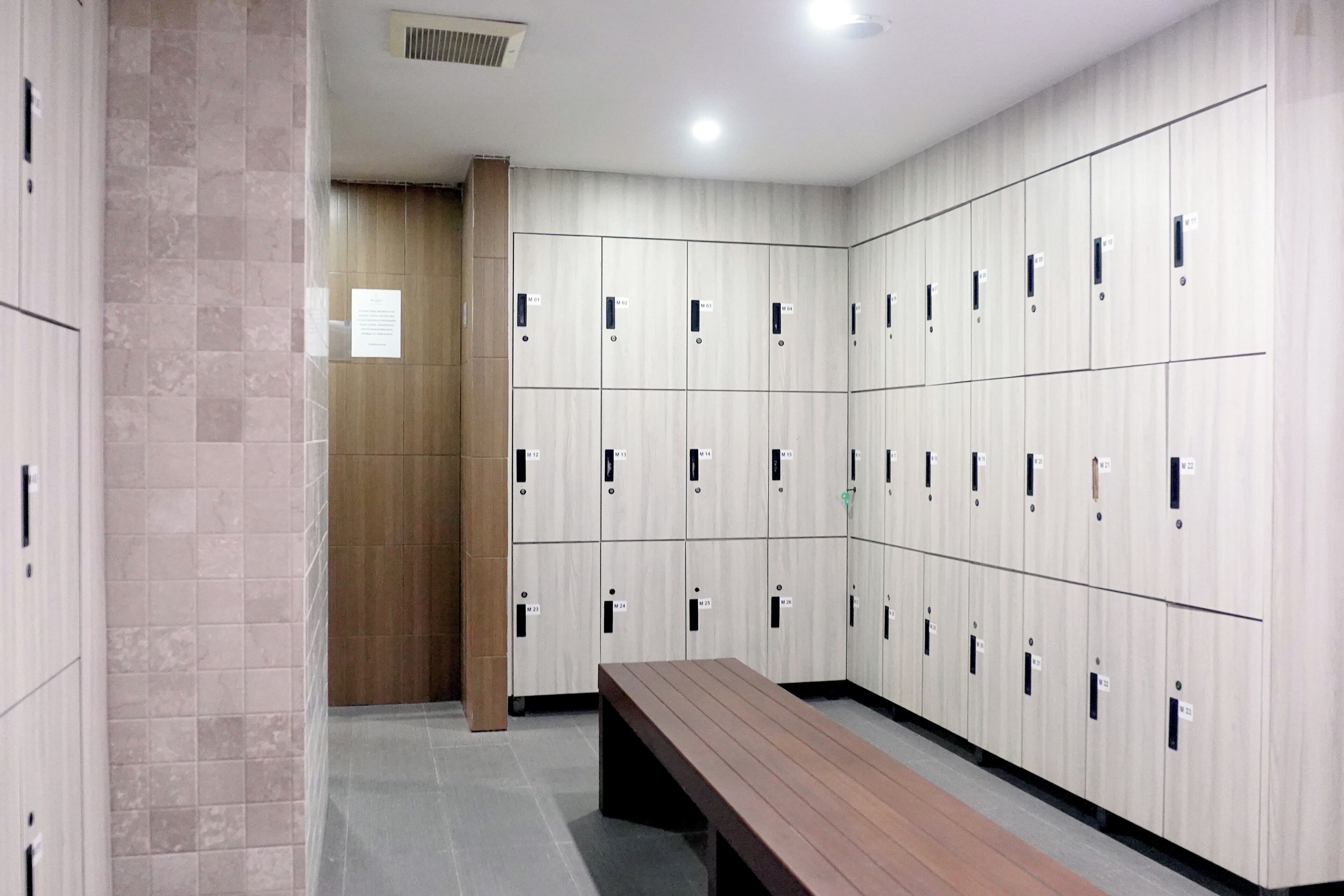 Eine Reihe von Schließfächern, in der Mitte eine Bank, ein gefliester Boden und im Hintergrund eine Holztür.