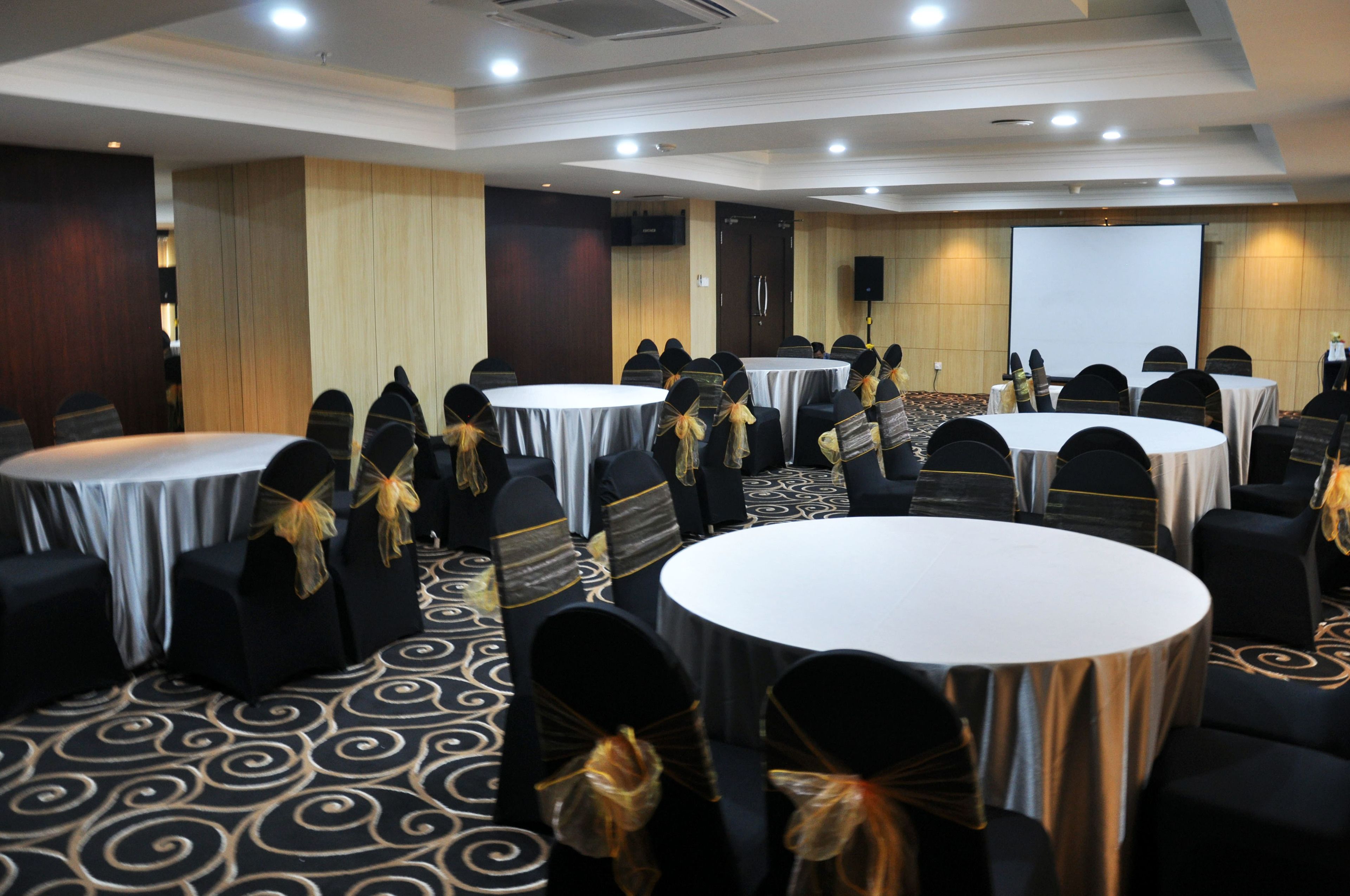 A conference room with round tables and chairs, equipped with a projector screen and a speaker.