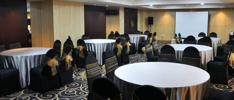 A conference room with round tables and chairs, equipped with a projector screen and a speaker.