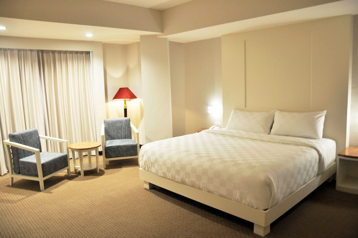 Une chambre d’hôtel avec un grand lit, deux fauteuils, une petite table et une lampe.