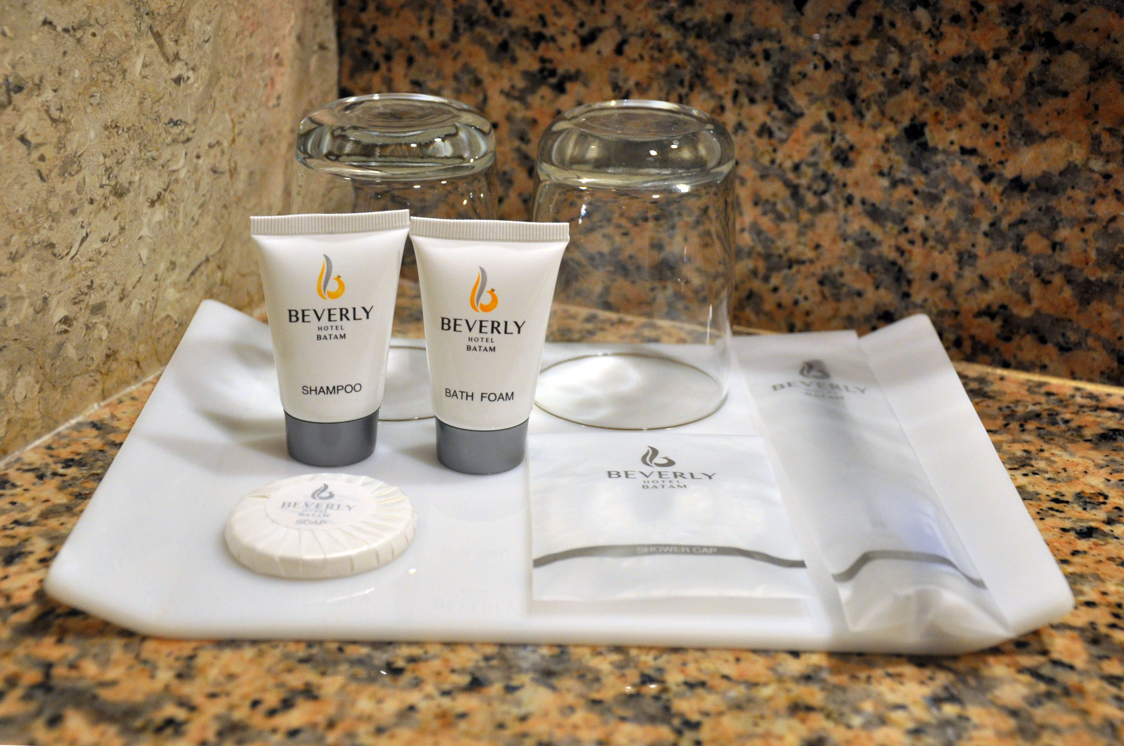 A tray with three Beverly Hotel toiletries: shampoo, bath foam, and a shower cap.