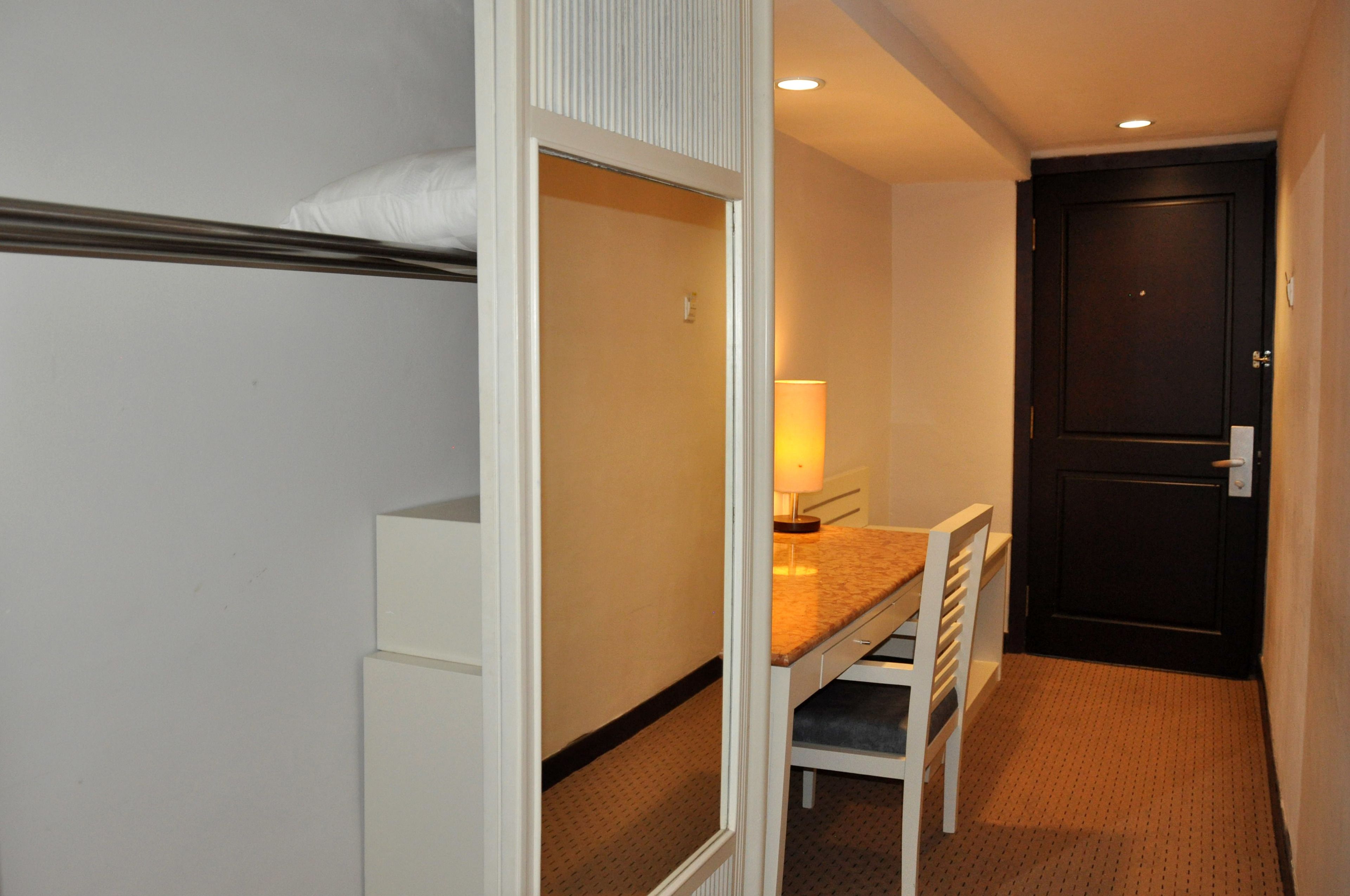 A compact hotel room with a bunk bed, a small desk with a chair, a lamp, and a door.