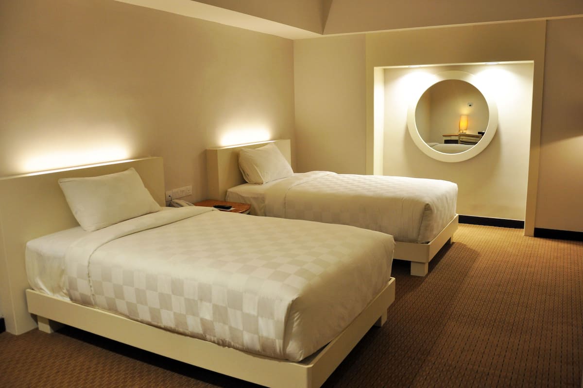 Une chambre d’hôtel avec deux lits, un miroir rond et une table de chevet avec une lampe.