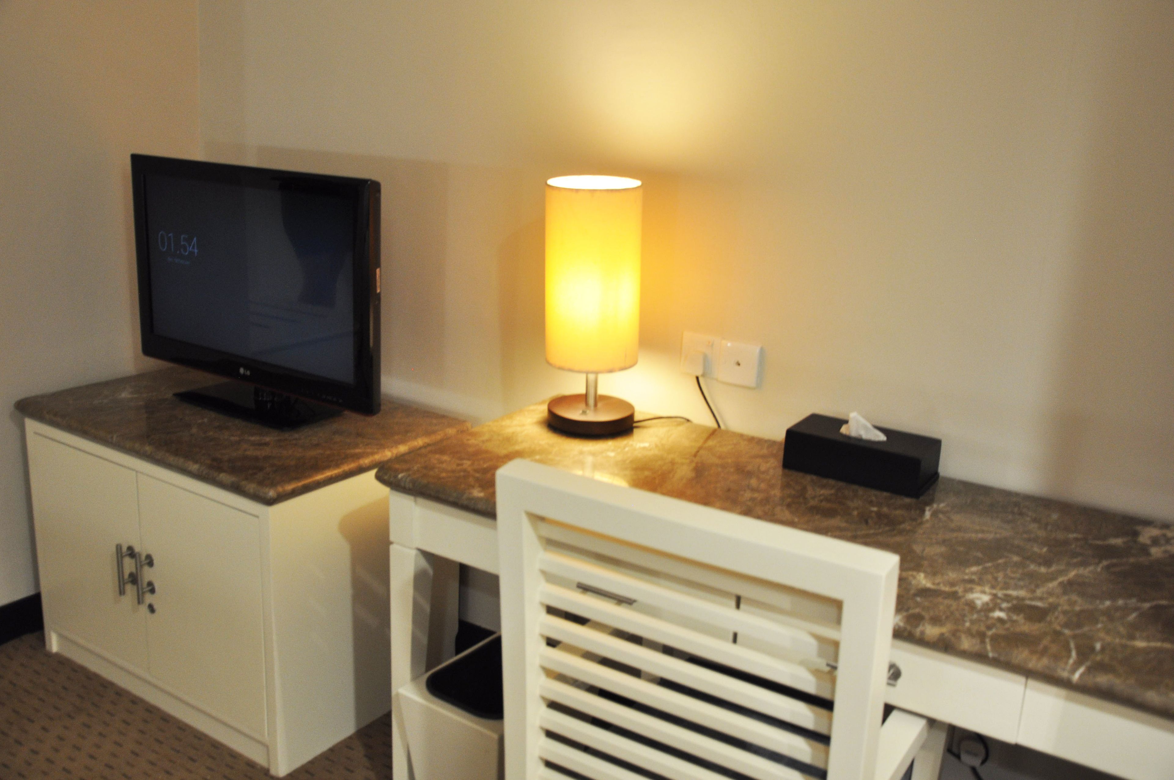 A hotel room with a TV on a cabinet, a lamp on the counter, and a tissue box.