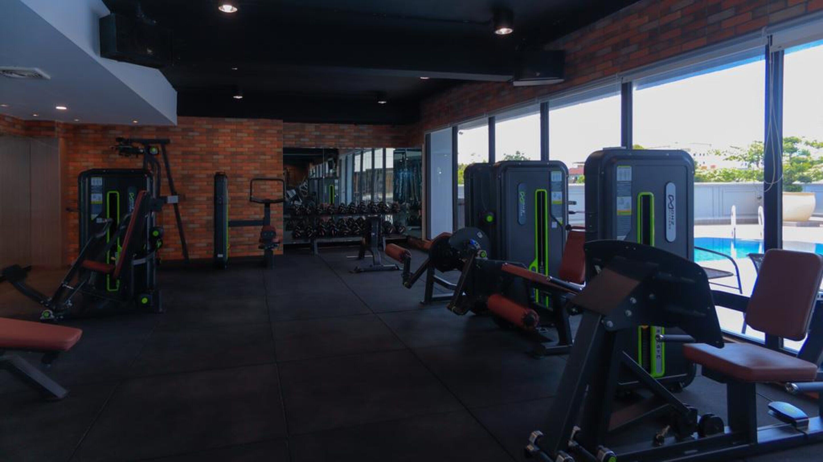 Une salle de sport équipée de divers appareils d’exercice, d’un banc et offrant une vue sur une piscine grâce à de grandes fenêtres.