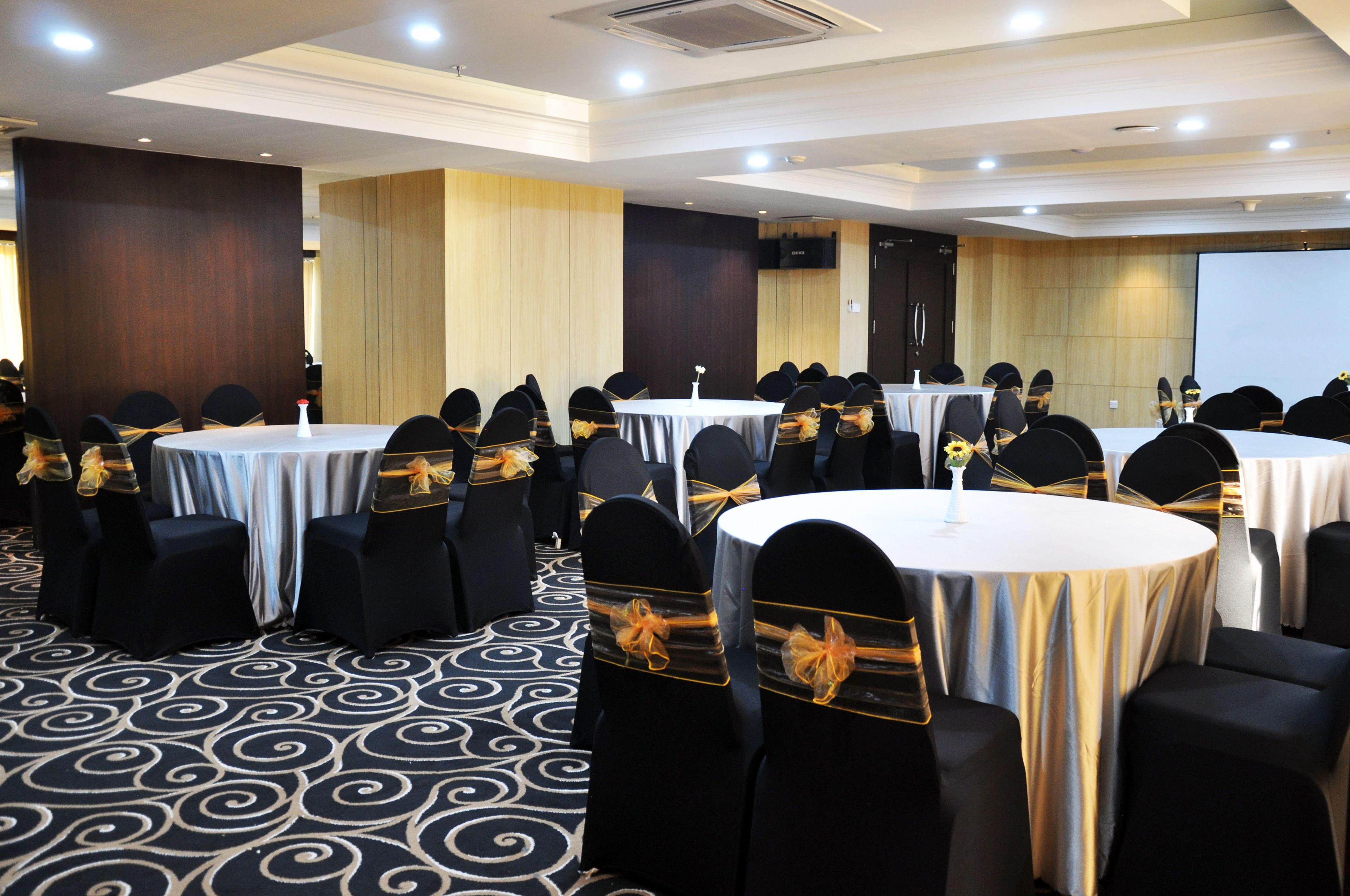 A conference room with multiple round tables, black chairs with gold sashes, and a patterned carpet.