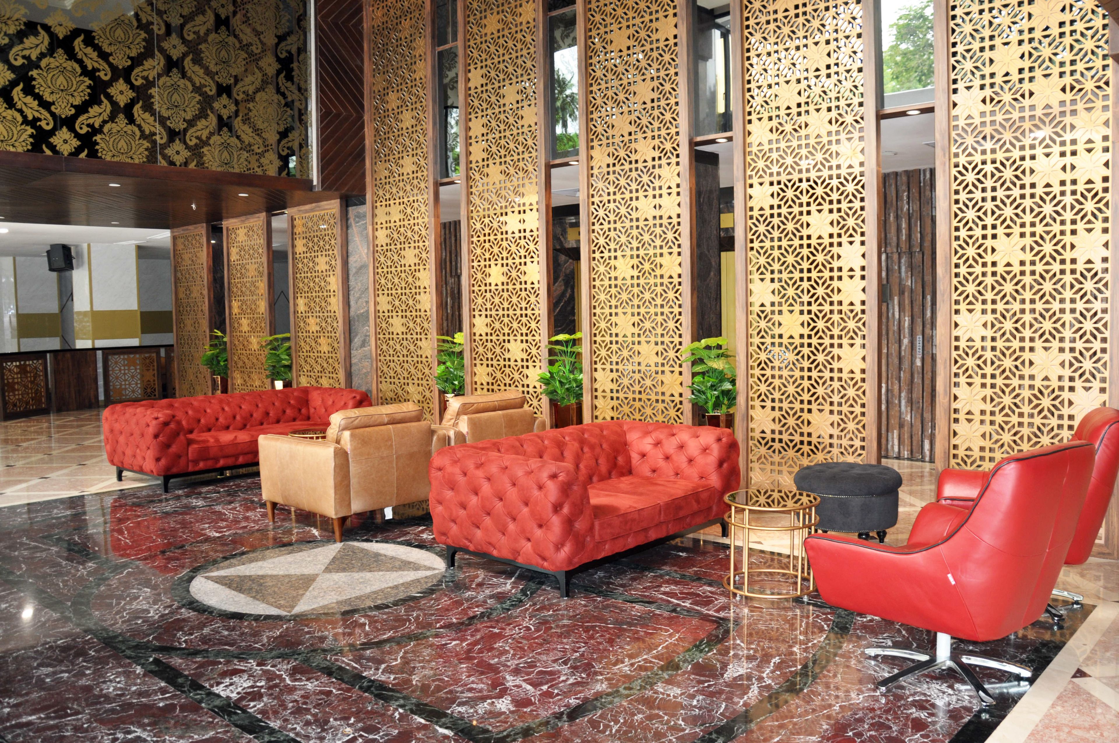 A lobby with red sofas, a red armchair, and a patterned wall.
