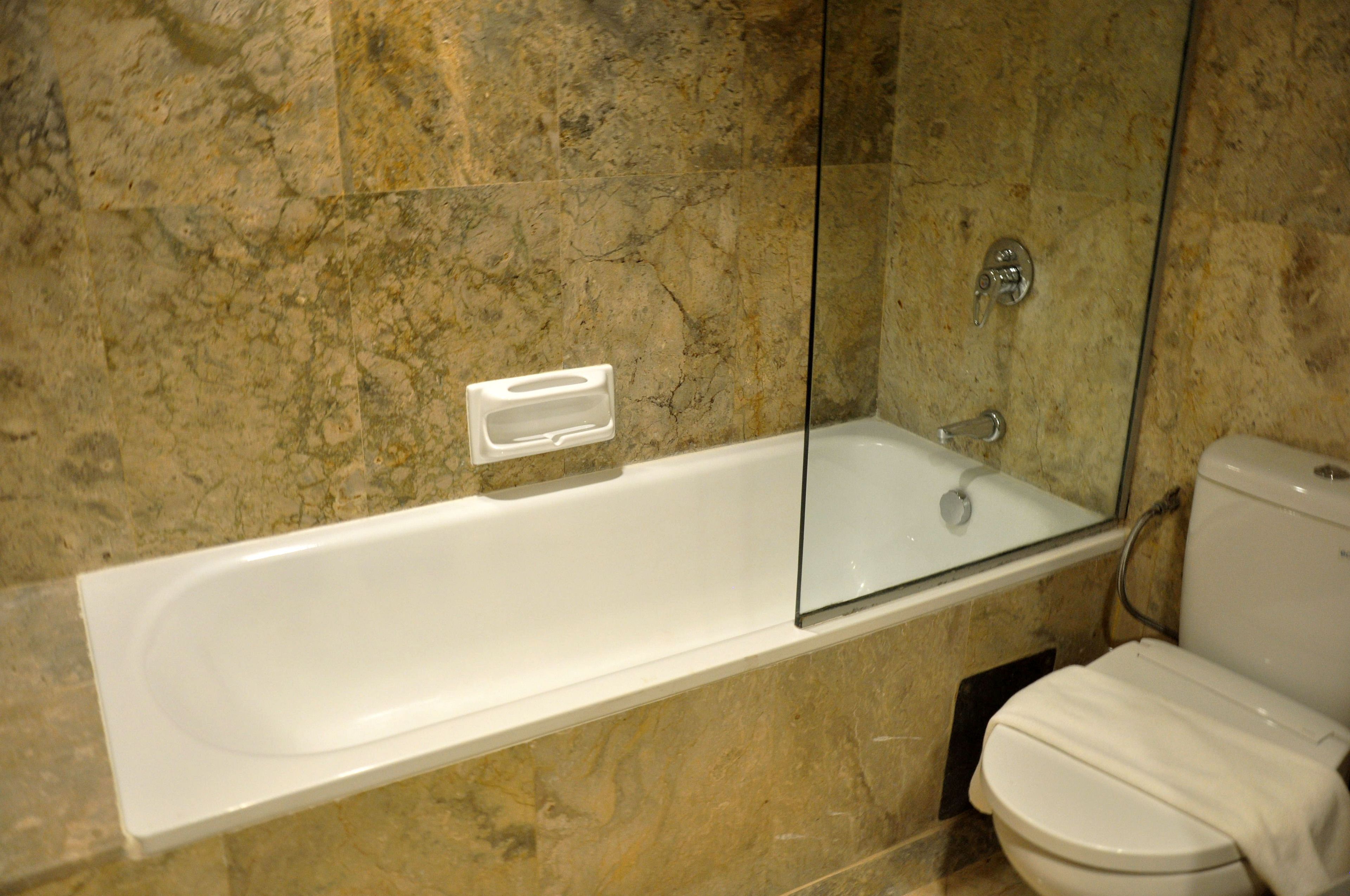 A bathroom with a bathtub, toilet, and marble walls.