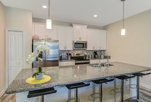 A modern kitchen with white cabinets, stainless steel appliances, a granite countertop, and a central island with bar stools.