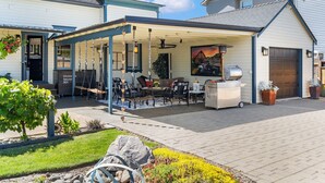A covered patio with outdoor furniture, a grill, and a painting of a vehicle. - Victorian Secrets 1897 Home - Curious? Eclectic, convenient & ❤️ of wine country (Newberg)