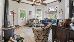 A cozy living room with a fireplace, patterned furniture, and a large window. - Victorian Secrets 1897 Home - Curious? Eclectic, convenient & ❤️ of wine country (Newberg)