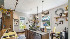 A kitchen with a central island, stainless steel appliances, pendant lighting, and a view through a window. - Victorian Secrets 1897 Home - Curious? Eclectic, convenient & ❤️ of wine country (Newberg)