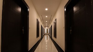Corredor comprido e estreito de um hotel, com portas de madeira escura em ambos os lados e chão de azulejos brilhantes.