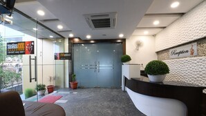 Uma área de recepção com porta de vidro, balcão de atendimento e plantas em vasos.