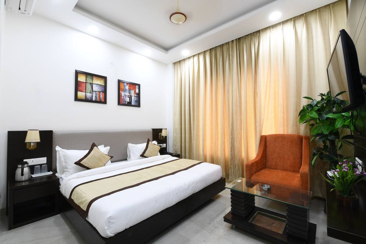 A hotel room with a large bed, a glass coffee table, a TV, and a plant.