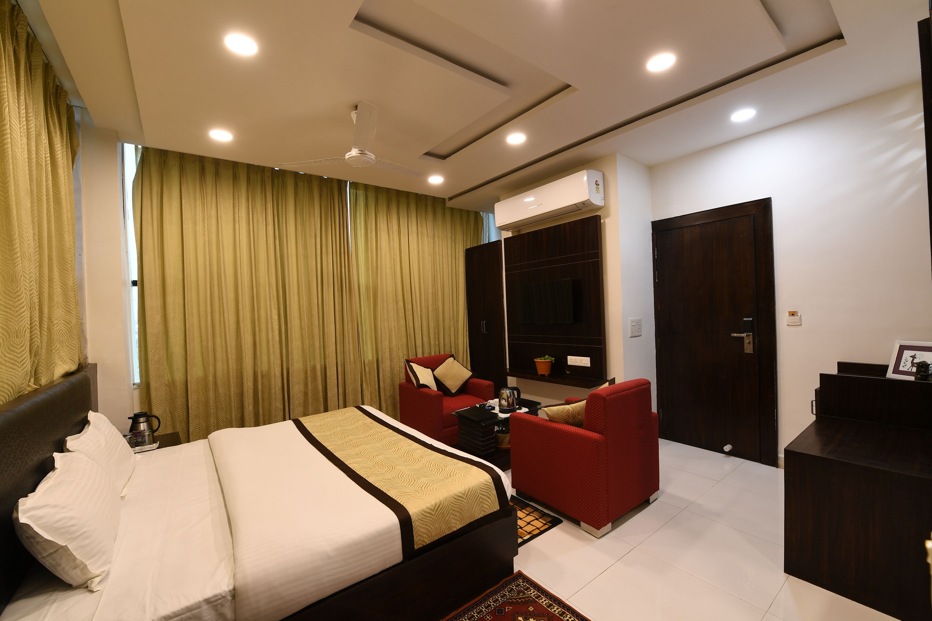 A hotel room with a bed, a red armchair, a desk, and a large window with curtains.
