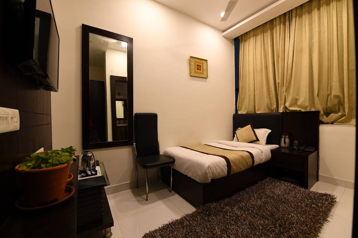 A modern bedroom with a bed, bedside table, chair, and a potted plant.
