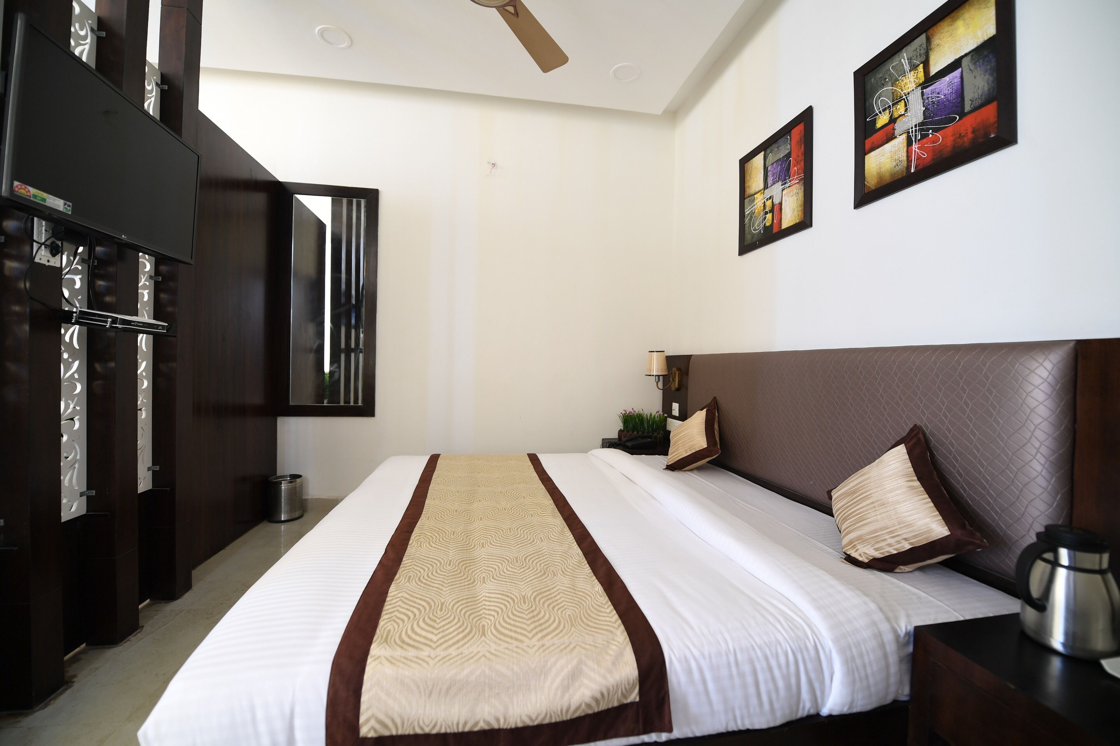 A hotel room with a large bed, a flat-screen TV mounted on the wall, a ceiling fan, and artwork on the walls.