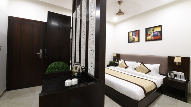 Quarto de hotel com uma cama grande, uma mesinha de cabeceira, uma cafeteira e um painel decorativo na parede.