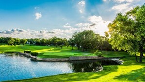Een golfbaan met een vijver, bomen en een heldere lucht.