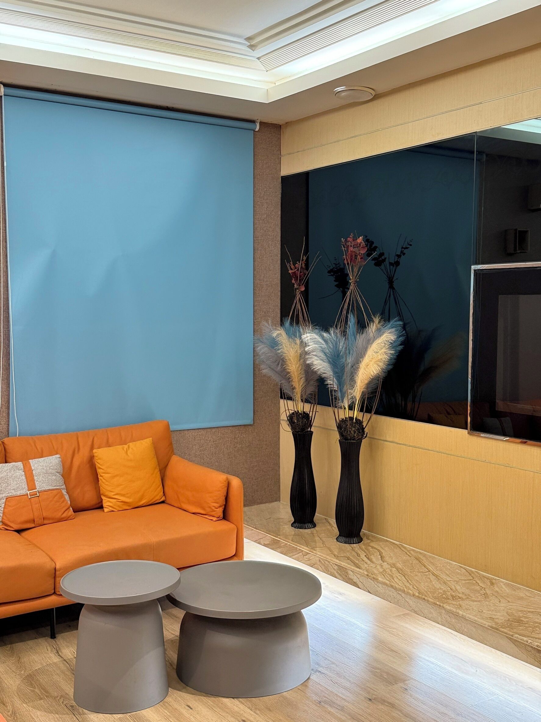Una sala de estar moderna con un sofá naranja, dos mesas auxiliares grises y jarrones decorativos con plantas.