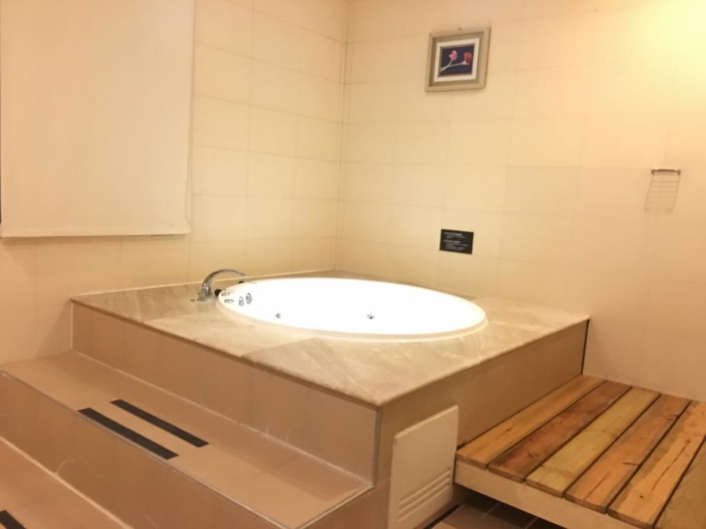 A bathroom with a large bathtub, a wooden bench, and tiled walls.